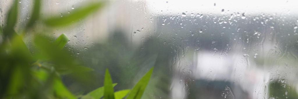 Rain against a window beside a softly lit room with a quiet, reflective mood.